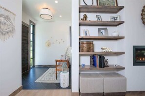 A modern living room with a fireplace, wooden shelves with decorative items, and a large window.