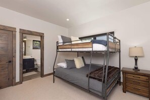 A bunk bed room with a wooden door, a small bedside table, and a view of the bathroom. - Luxury Big Sky Mountain Farmhouse (Big Sky)