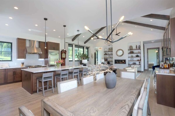 Una cocina moderna con una isla grande, iluminación colgante y vista al área de estar.