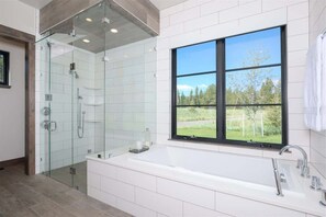 Un baño moderno con ducha de vidrio, una bañera grande y una ventana con vistas a zonas verdes.