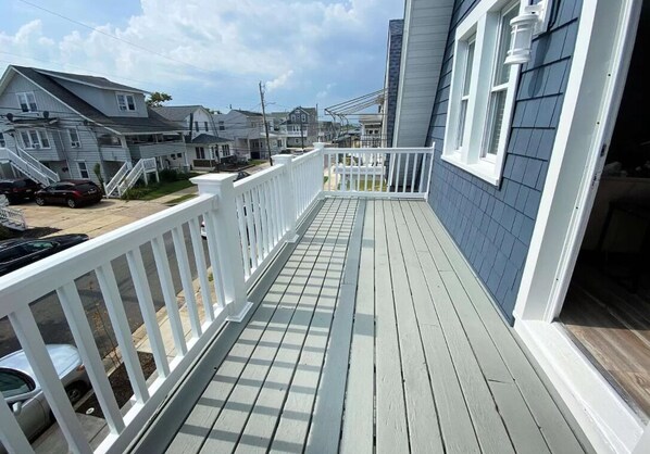 Een houten terras met witte leuningen, dat leidt naar een huis met blauwe bekleding en witte details.