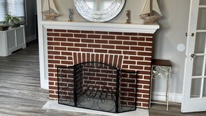 Una sala de estar con chimenea de ladrillo, un espejo redondo y dos pequeñas decoraciones de veleros.