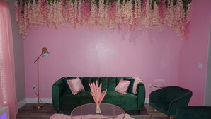 A room with a green velvet sofa, a pink fluffy rug, and a round glass coffee table. - Welcome to Gurl World Pink 2 bdr Loft (Houston)