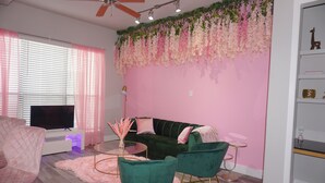A modern living room with a green sofa, pink chairs, a flat-screen TV, and a ceiling fan.