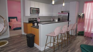 A modern kitchen with white cabinets, a stainless steel refrigerator, and a central island with bar stools. - Welcome to Gurl World Pink 2 bdr Loft (Houston)