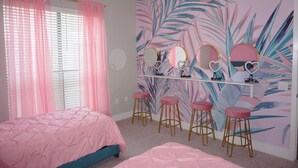 A bedroom with a pink bedspread, a vanity with mirrors and stools, and a tropical leaf-patterned wall. - Welcome to Gurl World Pink 2 bdr Loft (Houston)