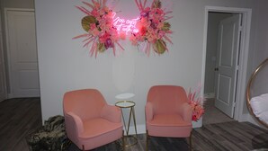 A room with two pink armchairs, a small white table, and a neon sign. - Welcome to Gurl World Pink 2 bdr Loft (Houston)