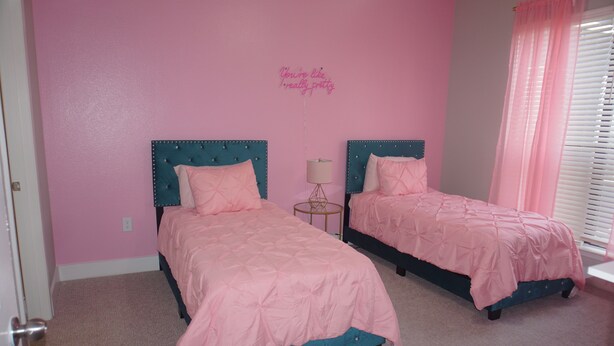 A bedroom with two beds, pink bedding, teal headboards, and a wall sign.