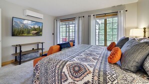 A bedroom with a large bed, a TV mounted on the wall, a window with curtains, and a wooden shelf. - Ridge Run Retreat (White Haven)