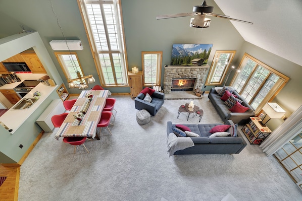 A spacious living room with a fireplace, a dining area with red chairs, and a kitchen with wooden cabinets.