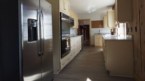 A modern kitchen with stainless steel appliances, wooden cabinets, and a tiled floor. - Golf & Hunting Retreat - Luxury Historic Barn Near Pinehurst (Southern Pines)