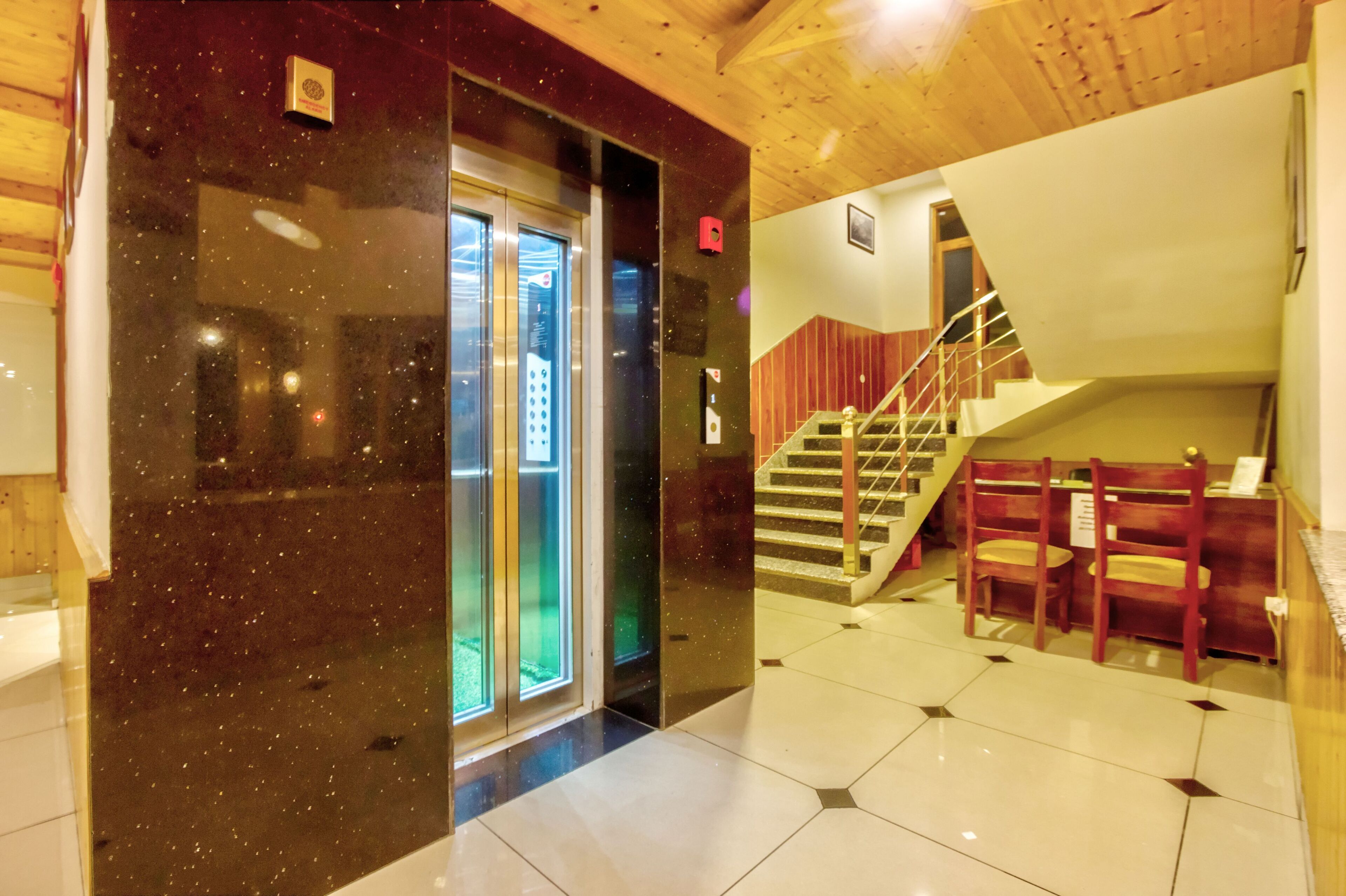A hotel lobby with a marble floor, a staircase, and wooden chairs.