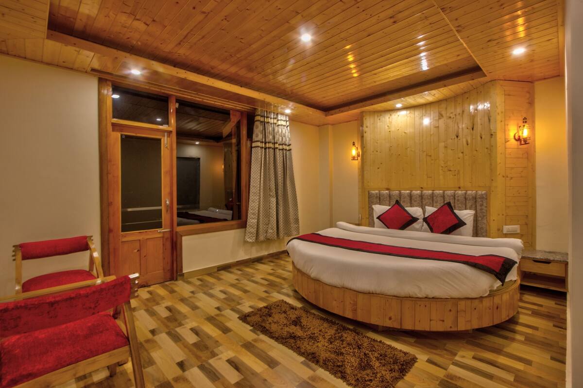 A bedroom with a round bed, wooden flooring, a red chair, and a window with curtains.