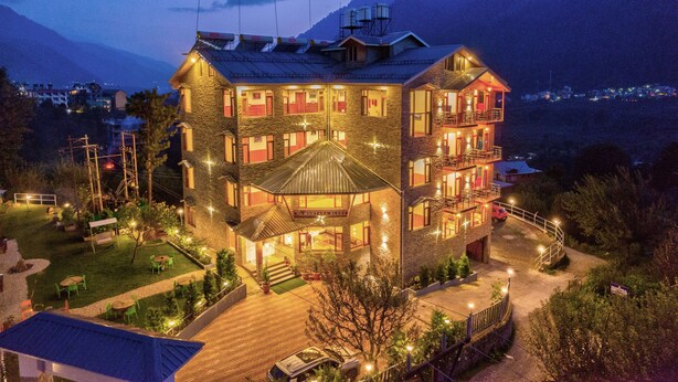 Un hotel de varios pisos con fachada de piedra, varios balcones y una entrada bien iluminada.