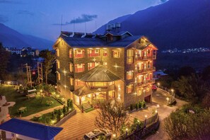 A multi-story hotel with a stone facade, multiple balconies, and a well-lit entrance. - Montana Blues Resort By Snow City (Manali)