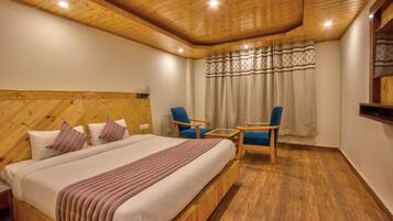 Una habitación con paneles de madera, una cama, dos sillas, una mesita y un ventanal con cortinas.