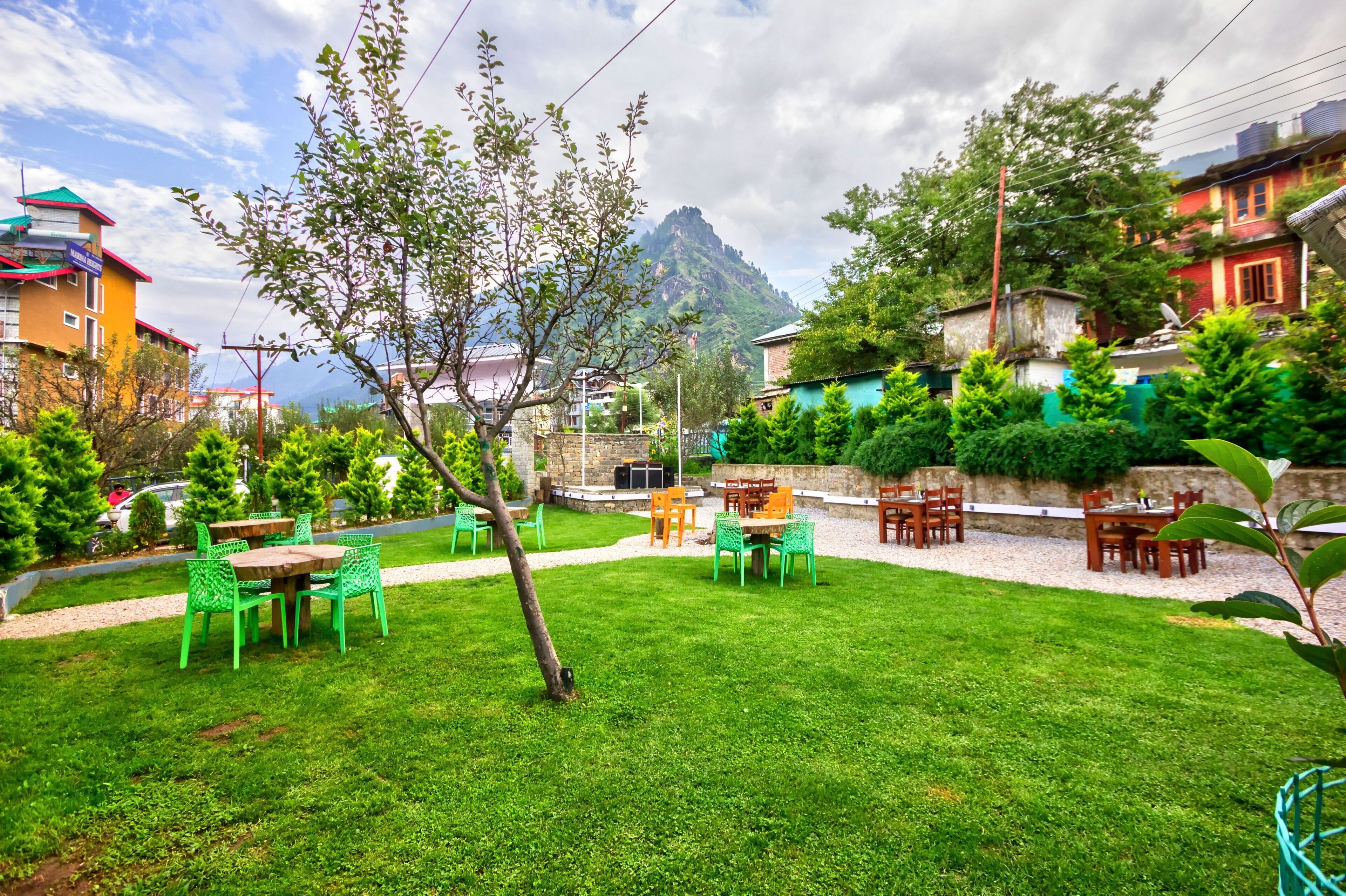 A well-maintained garden with outdoor seating, surrounded by residential buildings and a mountain in the background.