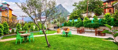 A well-maintained garden with outdoor seating, surrounded by residential buildings and a mountain in the background.