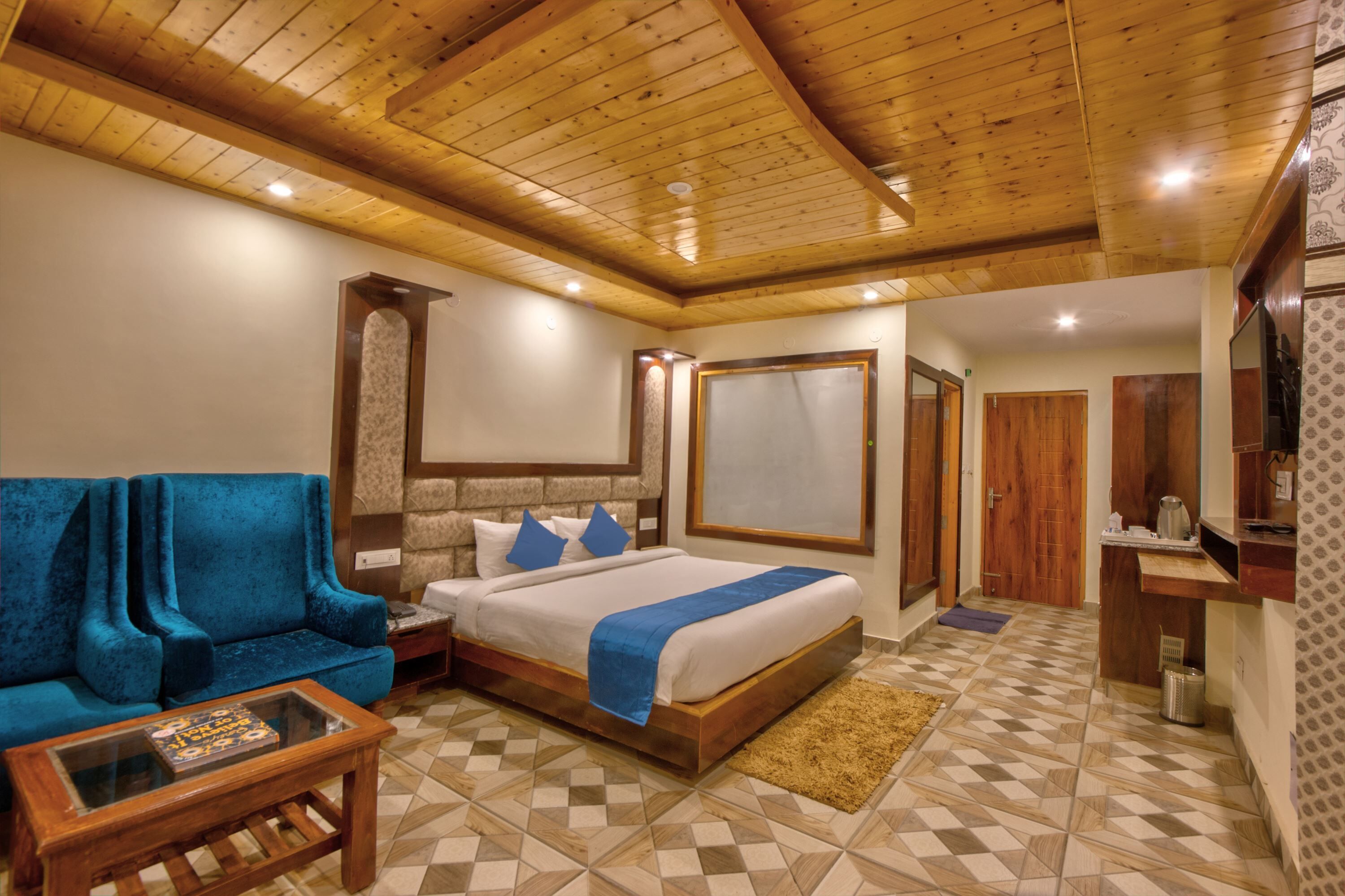 Un dormitorio con cama, sofá azul, mesa de centro de madera y alfombra estampada.
