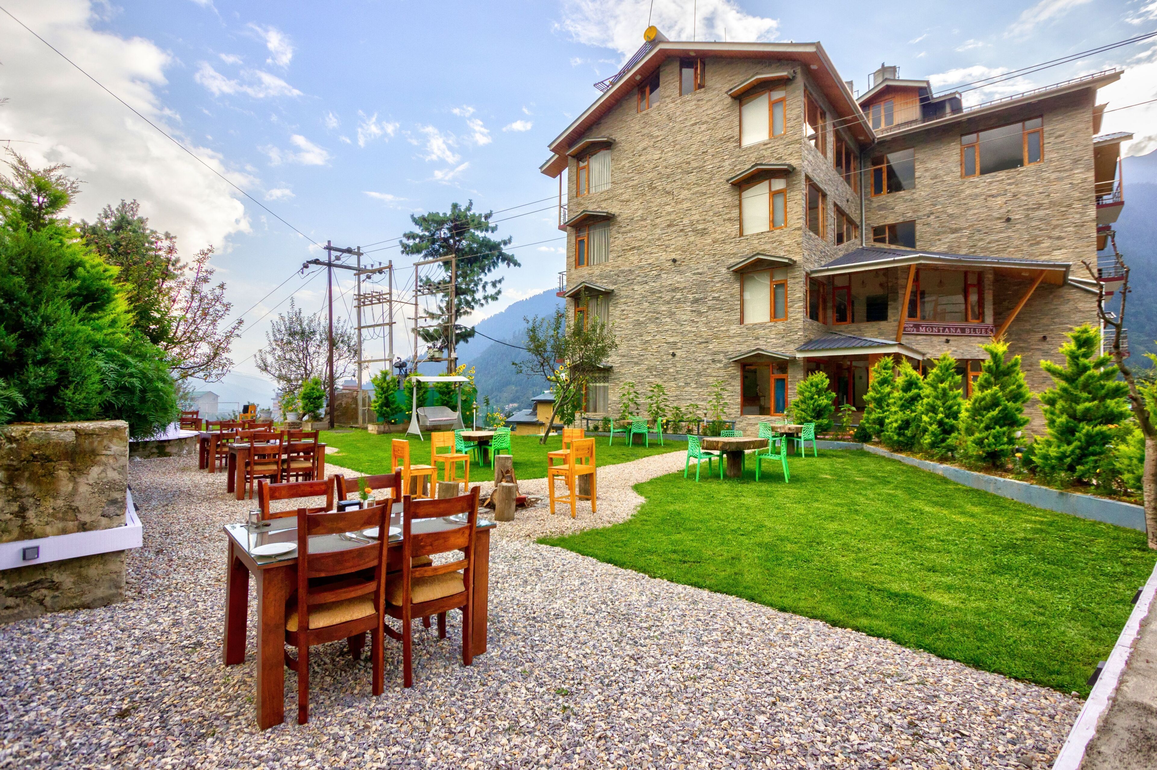 A multi-story building with a stone facade, outdoor seating area with tables and chairs, and a well-maintained lawn.