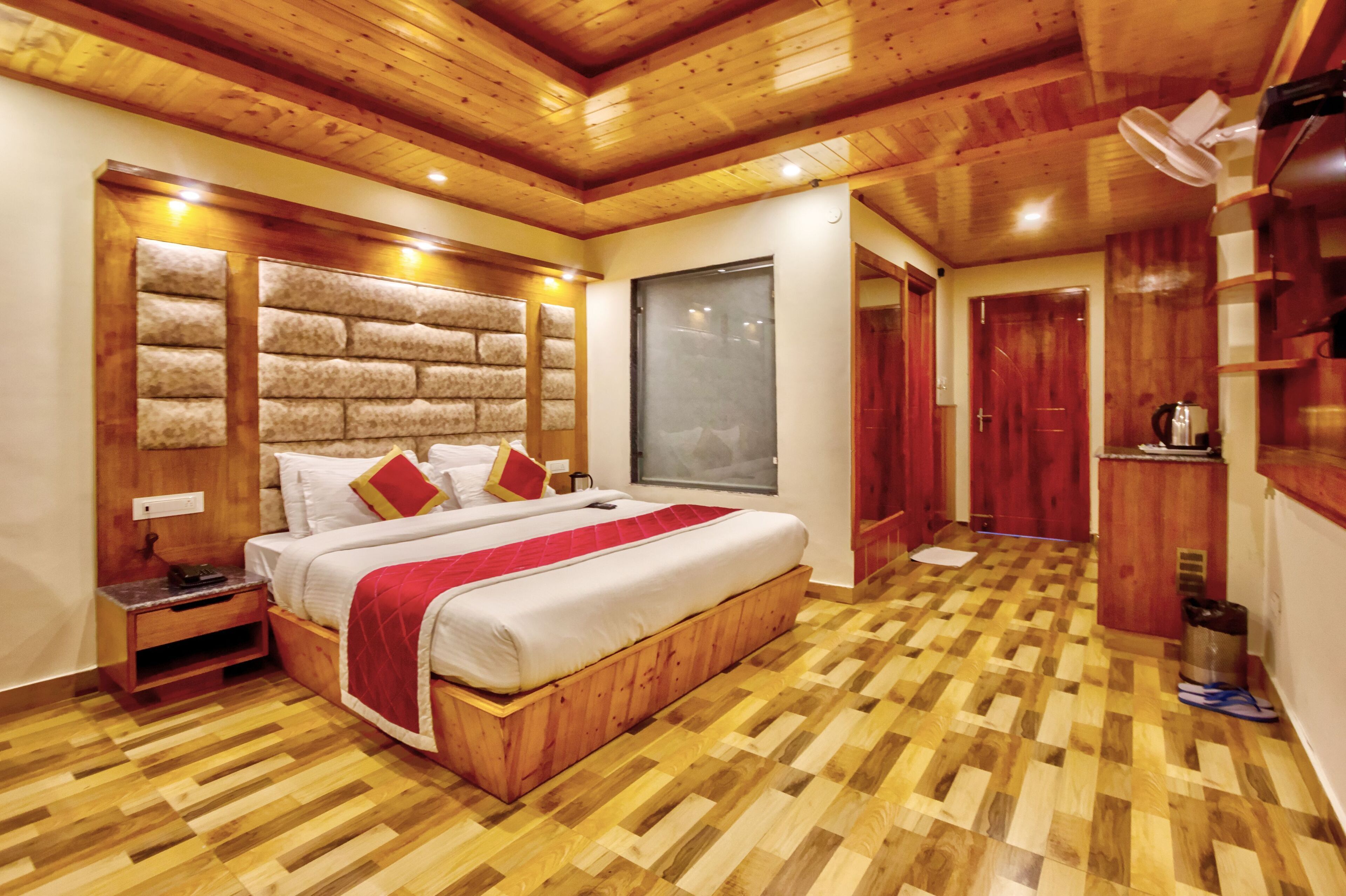 Une chambre à coucher avec une tête de lit en bois, un grand lit avec une literie rouge et blanche, un plancher en bois et une fenêtre.