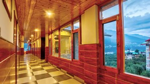 Un pasillo con suelo de tablones, paredes de madera y ventanas amplias con vistas a un paisaje montañoso.