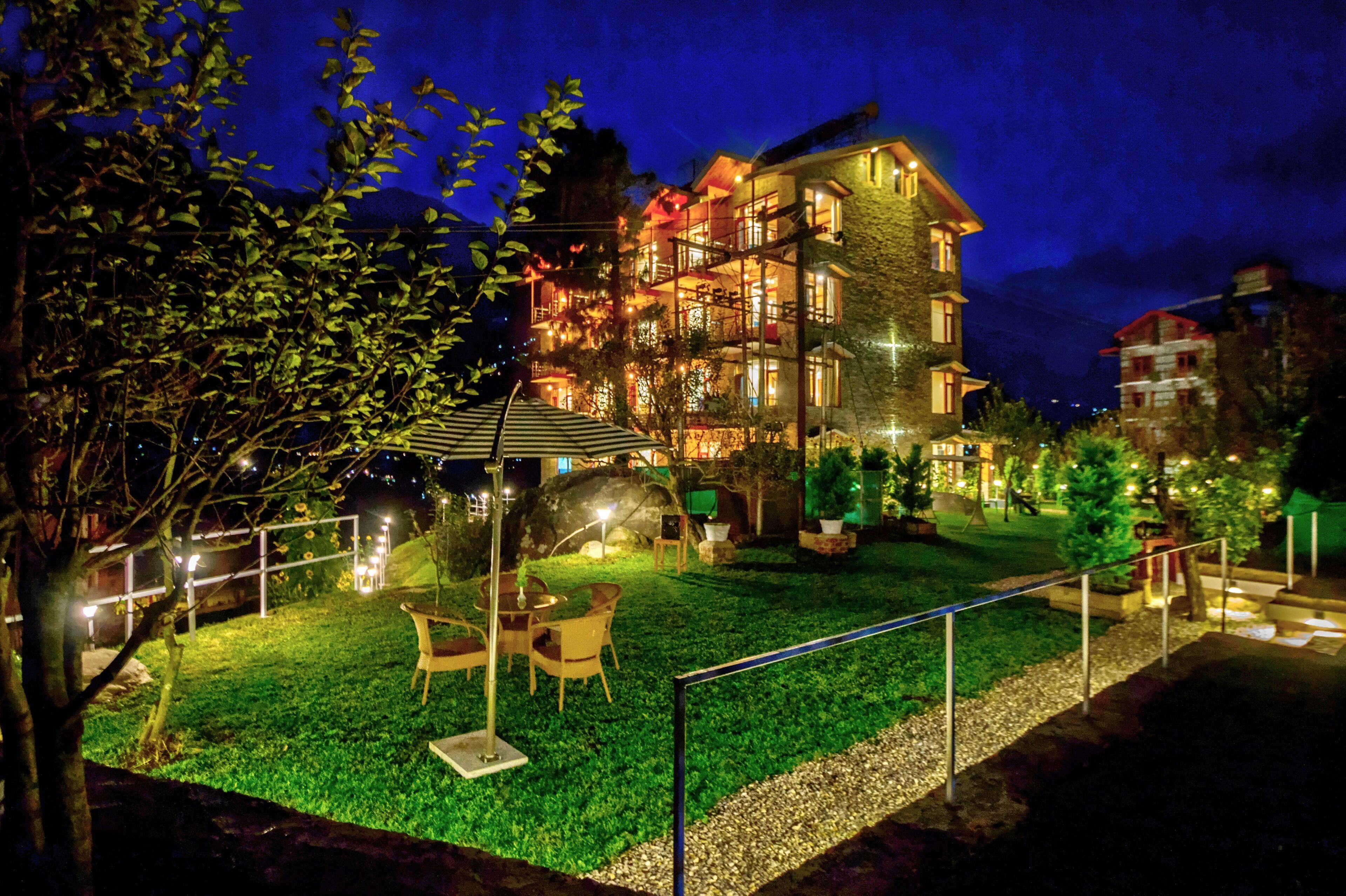 Un hotel de varios pisos con un área exterior bien iluminada, que incluye un césped y mobiliario.