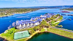 Un gran hotel con varias edificaciones a lo largo de una costa, una cancha de tenis y una carretera al lado del agua.