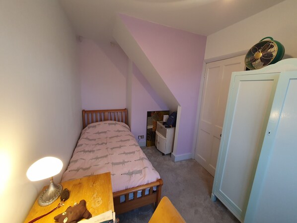 A bedroom with a bed, a bedside table with a lamp, a small desk with a chair, a wardrobe, and a door leading to another room. - Home away from home (Woking)