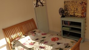 Une chambre avec un lit en bois, une table de chevet, un ventilateur et une tapisserie murale.