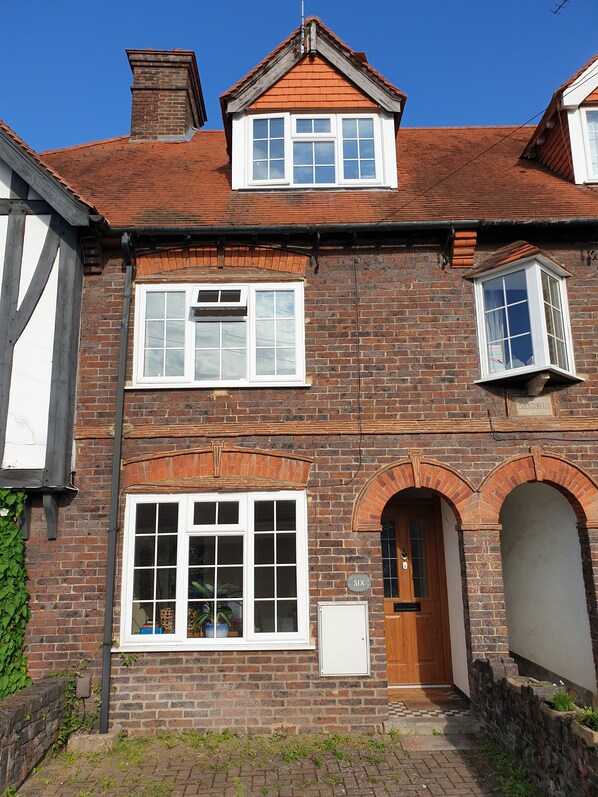 A two-story brick house with a wooden door, a visible number six, and a small garden area. - Home away from home (Woking)