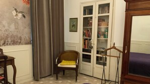 Une pièce avec un sol à carreaux, une chaise en bois dotée d’un coussin jaune, une bibliothèque et une armoire.