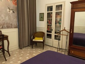 A room with a checkered floor, a wooden chair with a yellow cushion, a bookshelf, and a wardrobe.