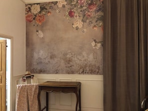 A room with a floral wallpaper, a small wooden table, and a door.
