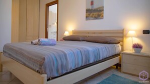 Un dormitorio con una cama, lámparas de noche, una mesita de noche, una planta en maceta y un cuadro de un faro en la pared.