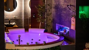 A modern spa area with a large bathtub, a mirror, and a small shelf with plants. - Suite-Designer-Whirlpool bath (Saint-Blimont)