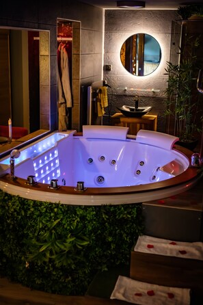 Un baño moderno con bañera de hidromasaje, espejo redondo y lavamanos pequeño.