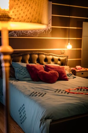 A bedroom with a tufted headboard, a bedside table with a lamp, and a bed with patterned bedding. - Suite-Designer-Whirlpool bath (Saint-Blimont)