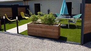 A modern outdoor patio area with a wooden planter, green chairs, a table, and a blue umbrella. - Suite-Designer-Whirlpool bath (Saint-Blimont)