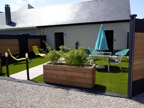 Un patio exterior moderno con una jardinera de madera, sillas verdes, una mesa y un paraguas azul.