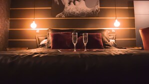 A bed with two champagne flutes, a red pillow, and a wall with horizontal lines and a large abstract painting. - Suite-Designer-Whirlpool bath (Saint-Blimont)