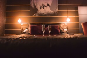 A bed with two champagne flutes, a red pillow, and a wall with horizontal lines and a large abstract painting. - Suite-Designer-Whirlpool bath (Saint-Blimont)
