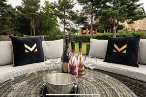 A round table with a metal bowl and wine glasses, two black pillows with gold chevrons, and wine bottles.