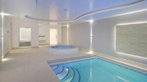 A modern indoor swimming pool with a starry ceiling, a hot tub, and a large window.
