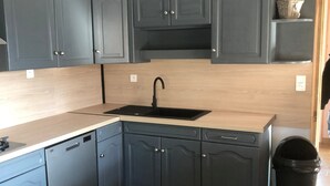 Una cocina con armarios grises, un lavamanos negro y una encimera de madera.