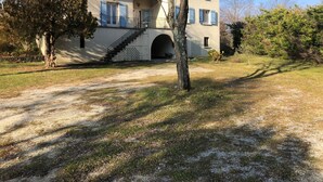 Una casa de dos pisos con una escalera que conduce a la entrada, rodeada de árboles y un cielo despejado.