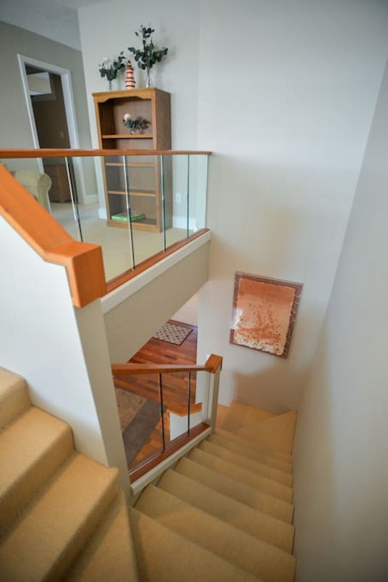 Un escalier avec une rampe en bois et des marches recouvertes d’une moquette beige, menant à un niveau inférieur.