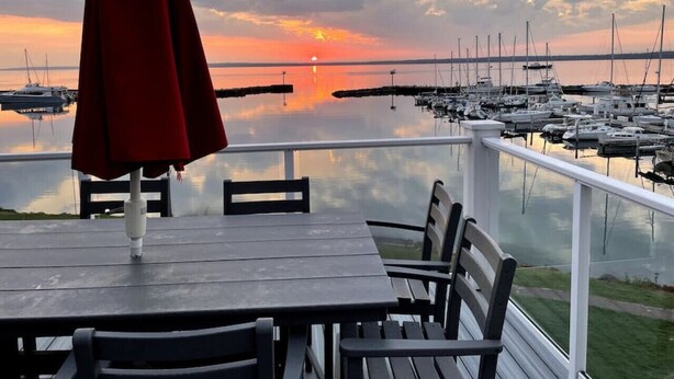 Een houten tafel en stoelen op een balkon met uitzicht op een jachthaven vol boten, onder een bewolkte lucht.
