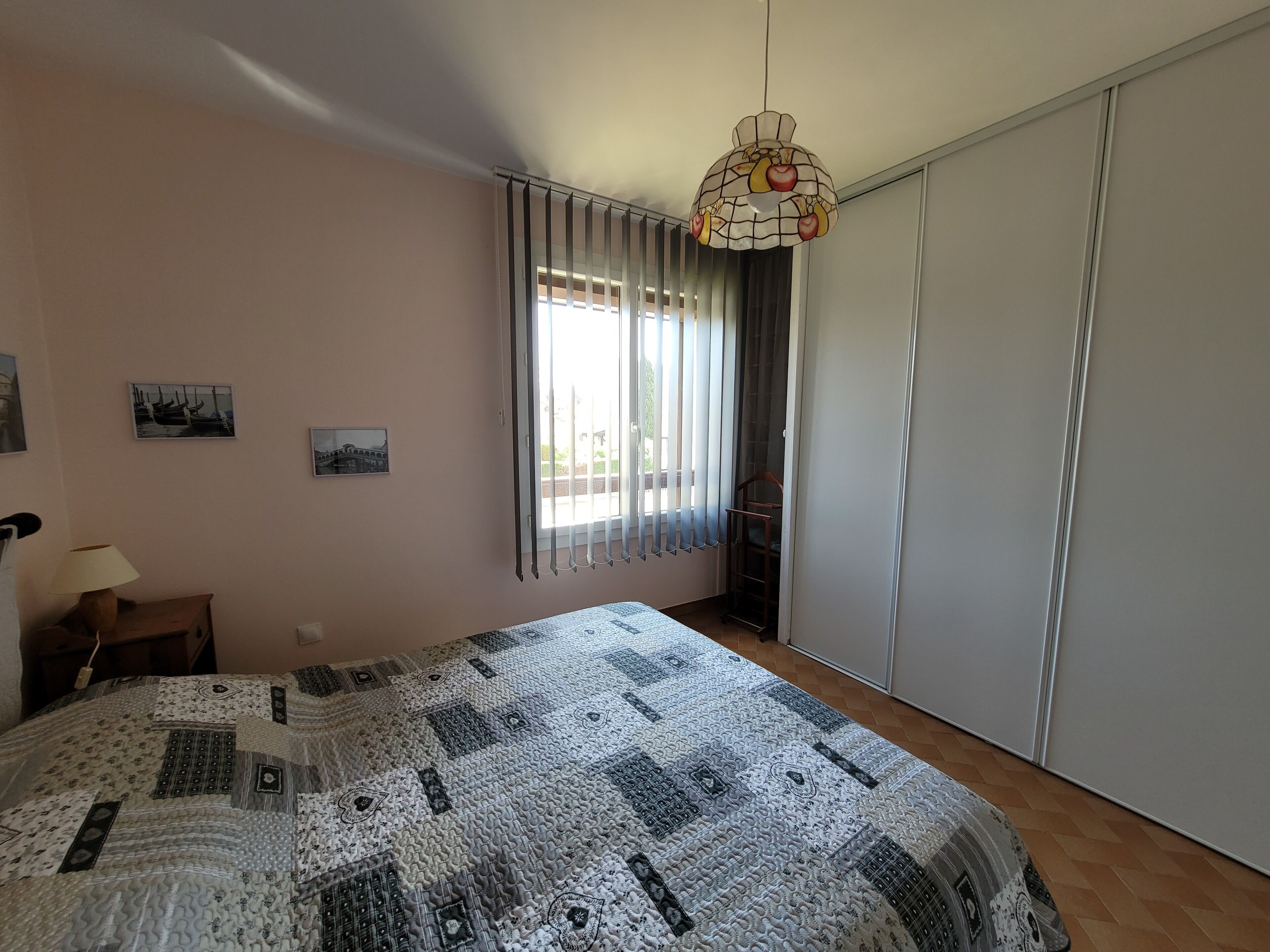 Un dormitorio con una cama grande, un candelabro colgante, una ventana con persianas y un armario.