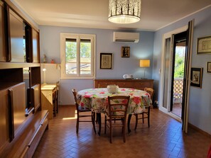Un coin repas avec une table dressée pour quatre personnes, un buffet en bois et une fenêtre donnant sur les arbres.